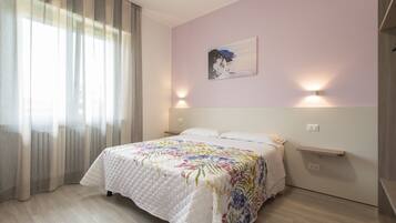 Een slaapkamer met een bed, een raam met gordijnen, een wandlamp en een schilderij.