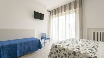 A hotel room with a bed, a chair, a TV mounted on the wall, and a window with curtains.