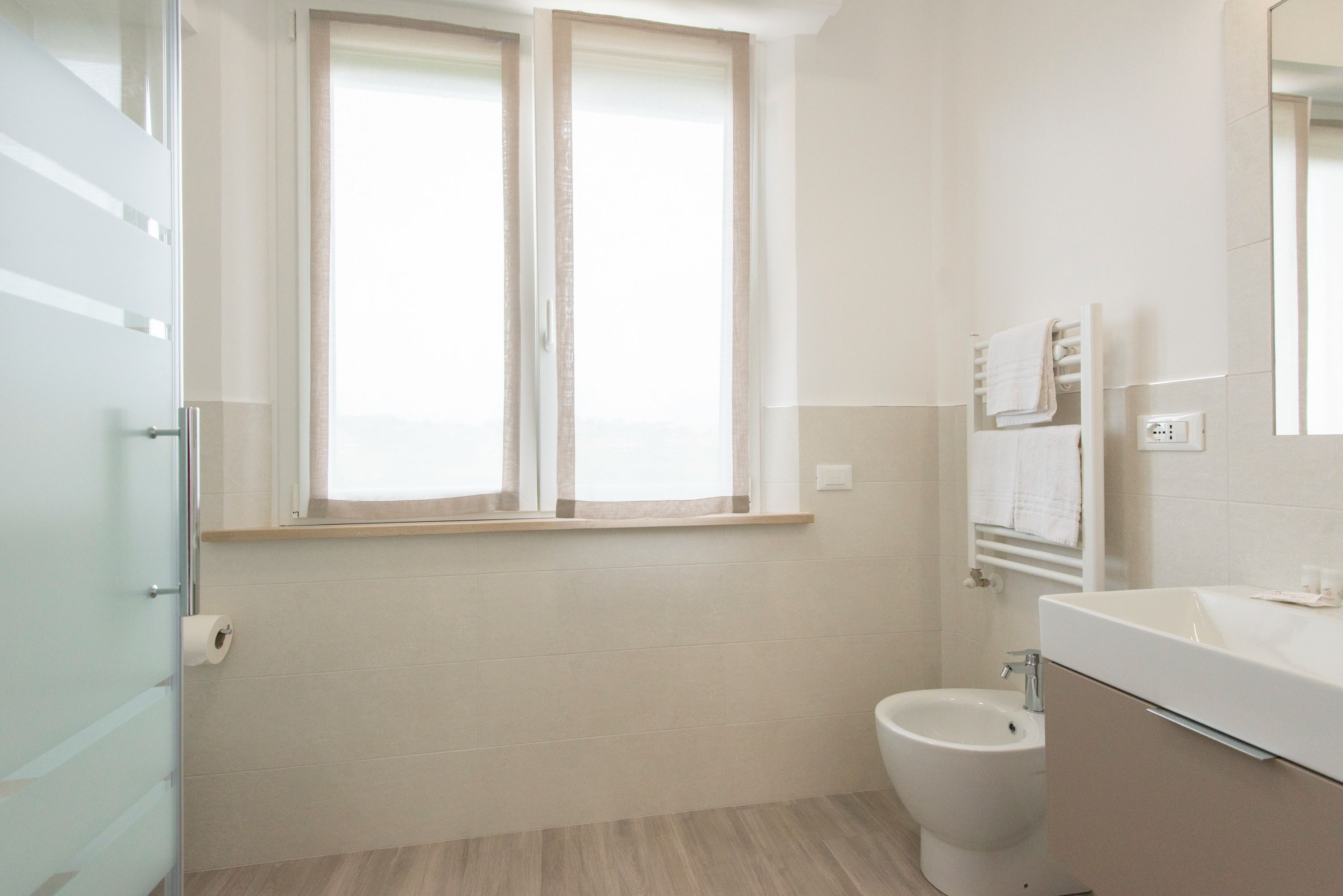 A bathroom with a toilet, a bidet, a sink, and a window with curtains.