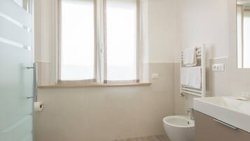 A bathroom with a toilet, a bidet, a sink, and a window with curtains.