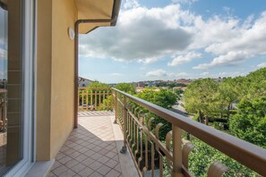 A balcony with a tiled floor, a metal railing, and a view of a residential area with trees and buildings. - Nel Conero affittacamere (Numana)