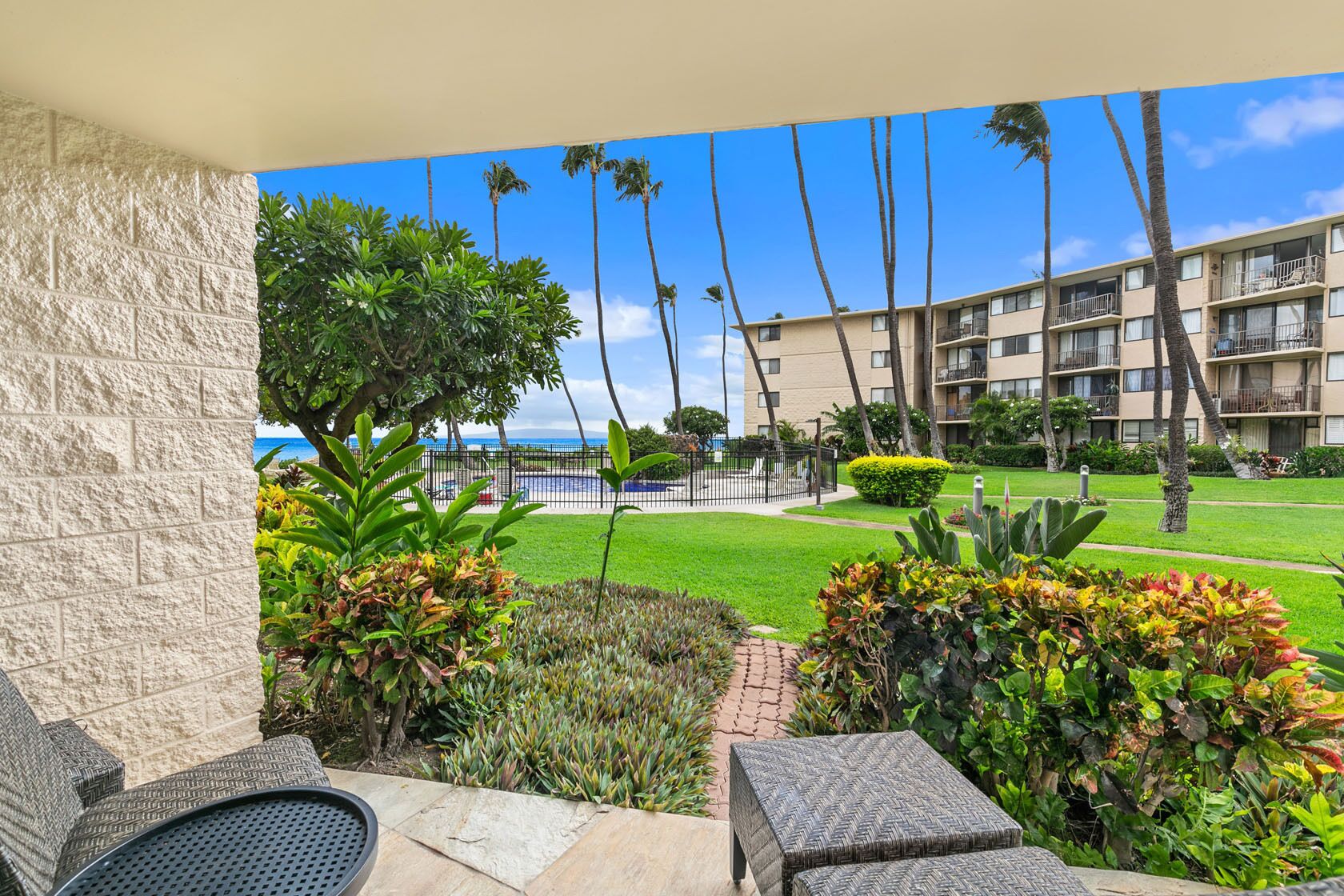 A hotel balcony with a view of the ocean, palm trees, and a well-maintained lawn.
