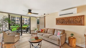 Ein großzügiges Wohnzimmer mit Sofa, Sesseln und Couchtisch. Ein großes Fenster bietet Blick auf einen Garten und einen Balkon.