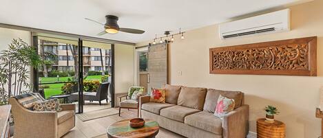 A spacious living room with a sofa, armchairs, and a coffee table. There is a large window with a view of a garden and a balcony.