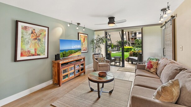Ein Wohnzimmer mit Fernseher, einer Holzunterhaltungseinheit und einem Sofa. Es gibt einen Balkon mit Gartenmöbeln.