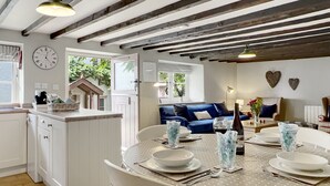 Una cocina moderna con armarios blancos, un comedor con mantel de lunares y un sofá azul en la sala de estar.