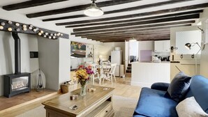 Una sala de estar con chimenea, vigas de madera, un sofá y una cocina al fondo.