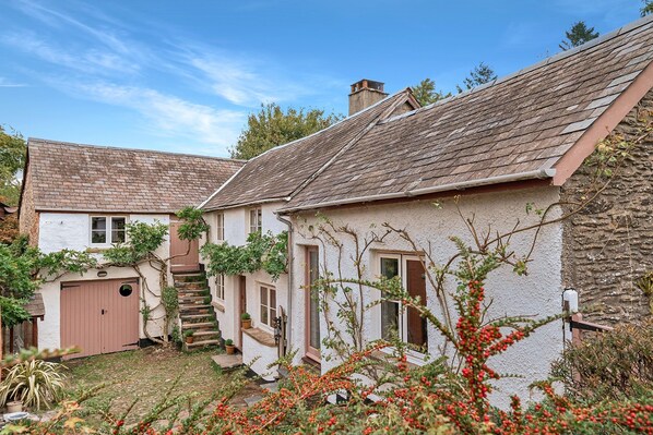 A traditional house with a stone facade, a wooden staircase, and a small garden with red berries. - The Old Malt House, Exton (Nr Dulverton)