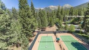 Una cancha de tenis al aire libre rodeada de árboles y montañas al fondo.