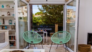 A cozy indoor patio with two green chairs, a glass table, and a wicker basket. - La Romana Triplex Apartment Javea Arenal, with Terrace, AC, Pool, Garden, Tennis (Javea / Xàbia)