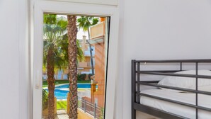 A bunk bed room with a window overlooking a swimming pool and palm trees. - La Romana Triplex Apartment Javea Arenal, with Terrace, AC, Pool, Garden, Tennis (Javea / Xàbia)