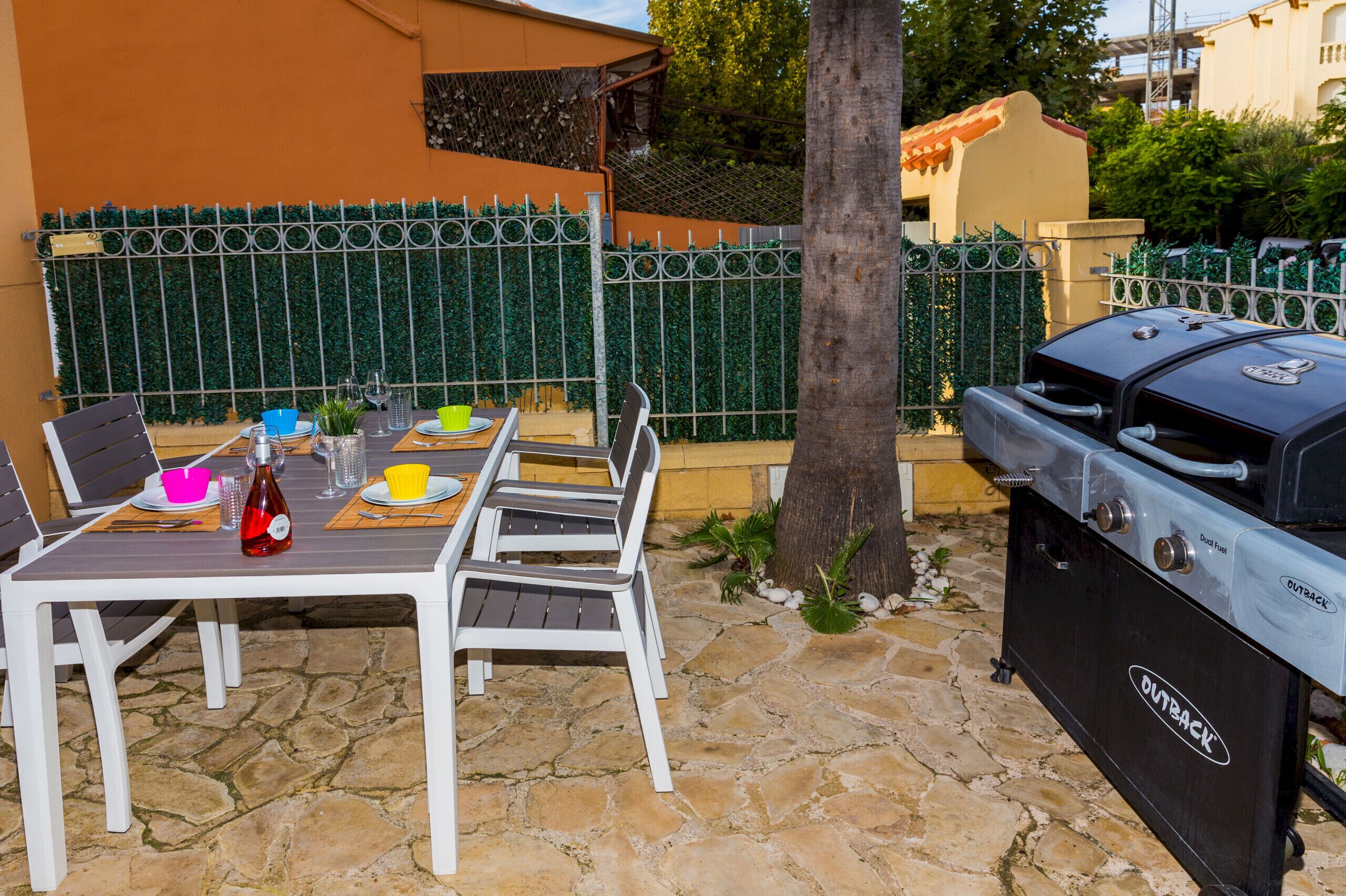 Ein Essbereich im Freien mit Steinboden, weißen Stühlen und einer Grillstation.