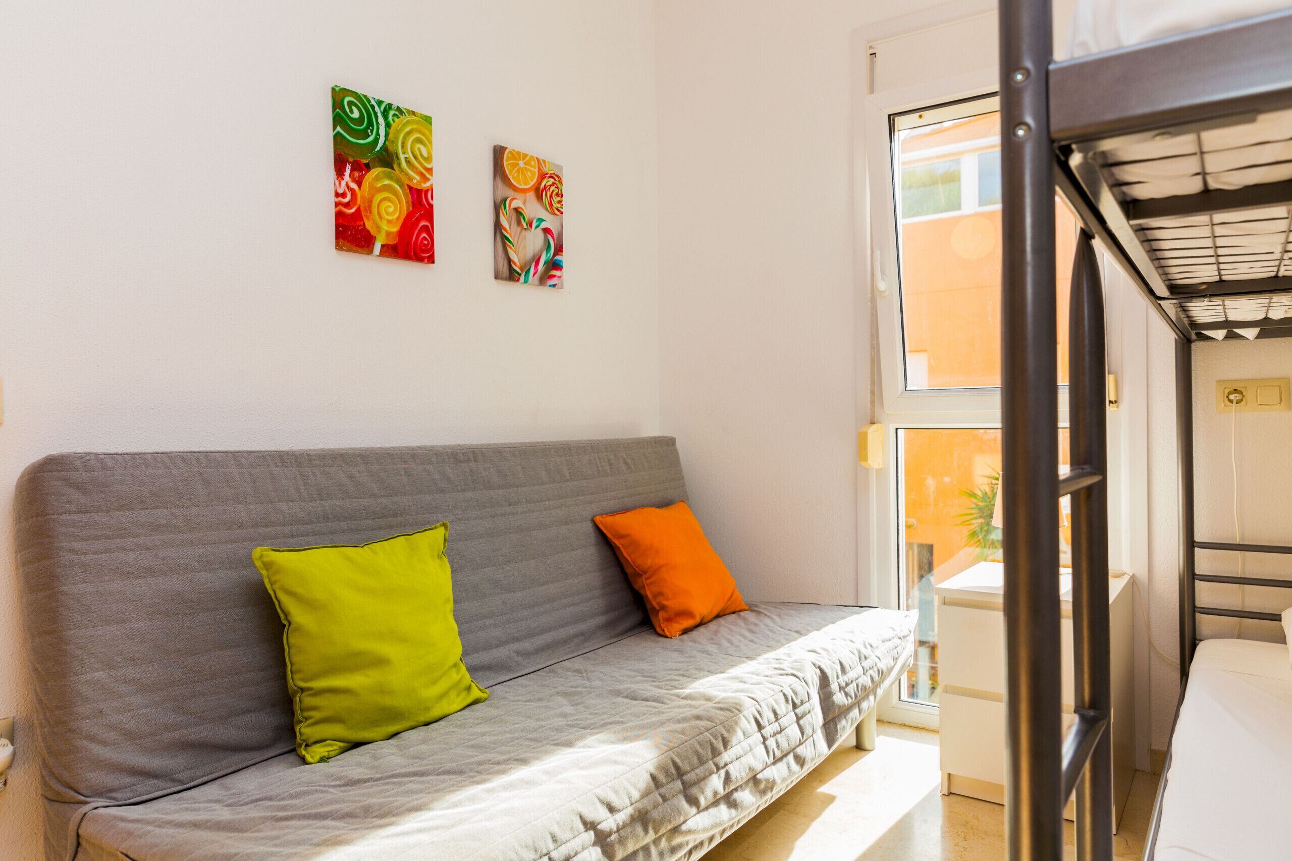 A grey sofa with two pillows, a window, and two wall art pieces.