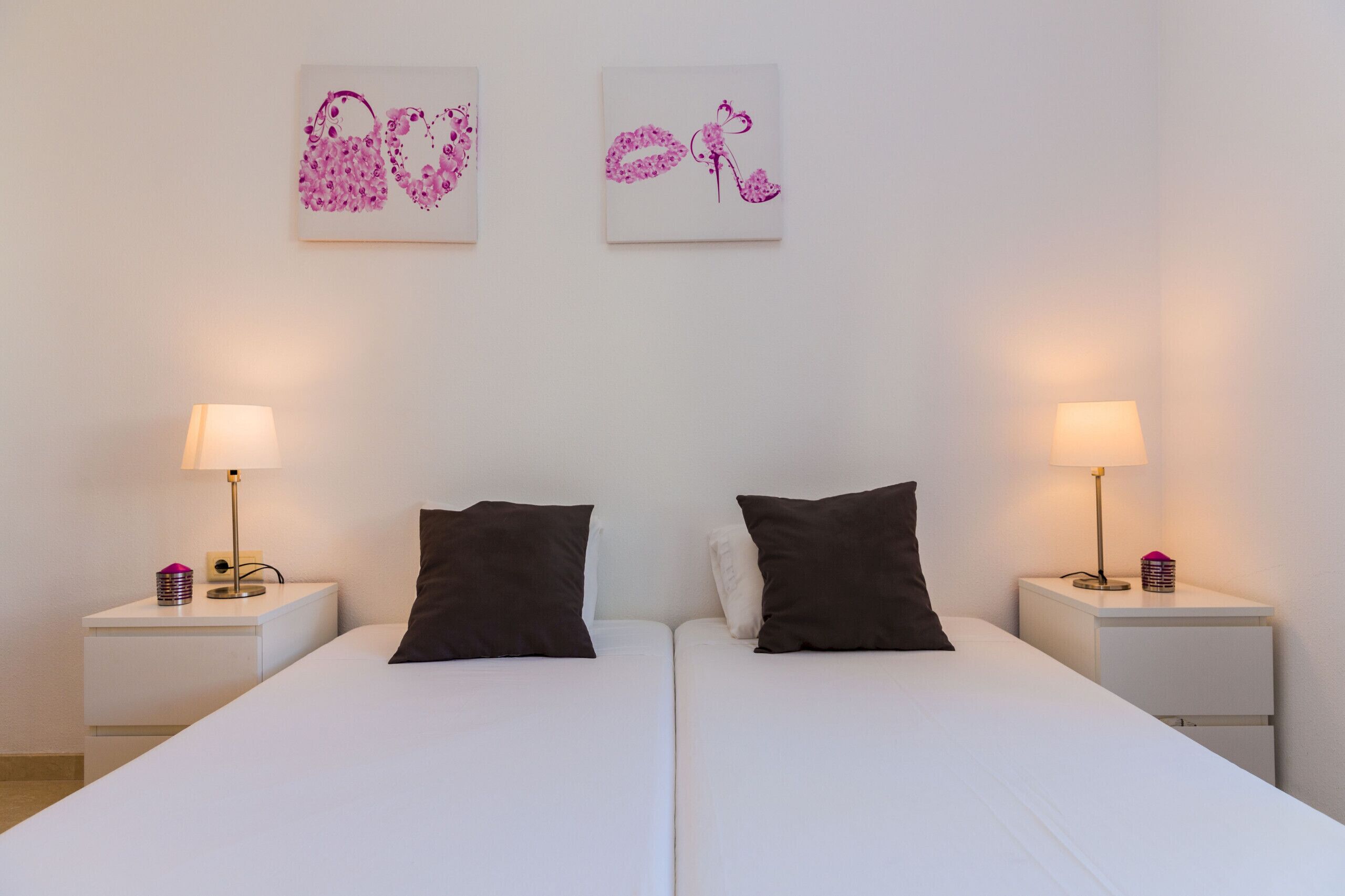 Un lit double avec deux oreillers noirs, une tête de lit blanche et deux tables de chevet ornées de lampes et d’objets décoratifs.