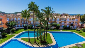 A swimming pool with a curved design, surrounded by palm trees and a well-maintained lawn. - La Romana Triplex Apartment Javea Arenal, with Terrace, AC, Pool, Garden, Tennis (Javea / Xàbia)