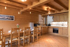 A wooden interior with a dining table and chairs, a kitchen with wooden cabinets, and a tiled floor.