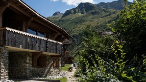 Eine Holzhütte mit Steinunterbau, einem Balkon mit Holzgeländer und einem Berg im Hintergrund.