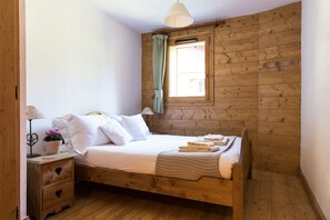 Une chambre à coucher aux murs lambrissés, comprenant un lit, des tables de chevet, une fenêtre avec des rideaux et un luminaire suspendu.