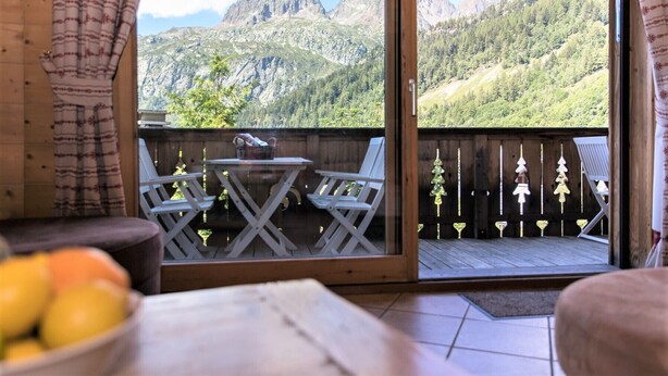 Ein Balkon mit Tisch und Stühlen, ein Holzzaun und Blick auf die Berge.