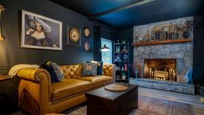 A cozy living room with a leather sofa, a stone fireplace, and a bookshelf filled with decorative items. - walk to square! Cozy 2 BR bungalow, moody design (Dahlonega)