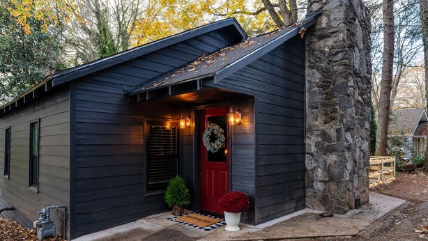A small cabin with a dark exterior, a red door, and a stone pillar. - walk to square! Cozy 2 BR bungalow, moody design (Dahlonega)