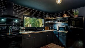 A modern kitchen with black cabinetry, a built-in microwave, and a refrigerator. - walk to square! Cozy 2 BR bungalow, moody design (Dahlonega)
