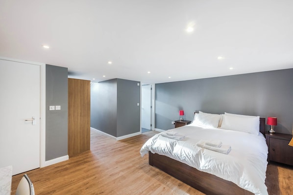 A modern bedroom with a large bed, wooden flooring, and a grey accent wall.