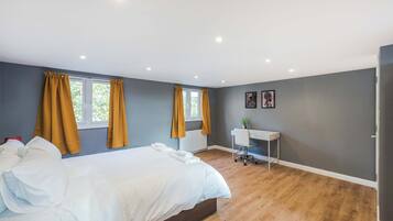 Un dormitorio moderno con una cama grande, dos ventanas con cortinas, un escritorio y un radiador.