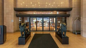A hotel entrance with a glass door, two lion statues, a tiled floor, and a metal cart.