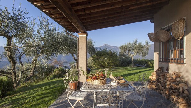 An outdoor patio with a table set for dining, surrounded by stone walls and a view of mountains. - Casa Pedona (Camaiore)
