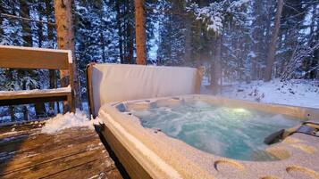 Un jacuzzi rodeado de árboles cubiertos de nieve, con una terraza de madera al frente.