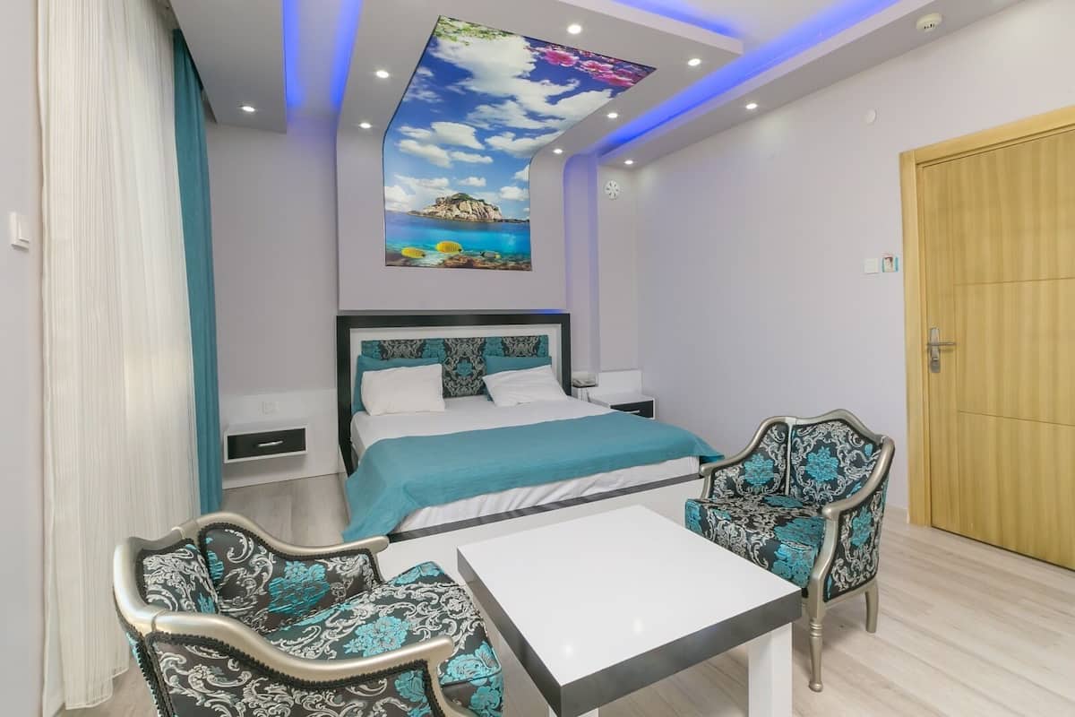 A modern bedroom with a bed, two chairs, a table, and a ceiling mural.