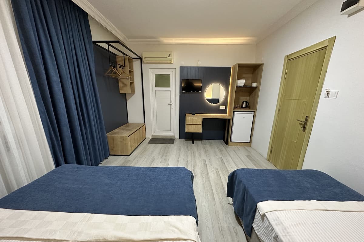 A hotel room with two beds, a desk, a wardrobe, and a small kitchenette.