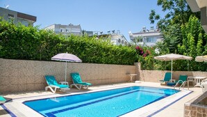 A swimming pool with lounge chairs and umbrellas, surrounded by a stone wall and greenery. - Enda Lara Hotel (Antalya)