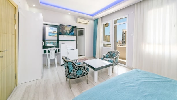 A modern hotel room with a bed, two chairs, a small table, a desk with a computer, a TV, and a wardrobe. - Enda Lara Hotel (Antalya)