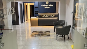 A hotel reception area with a reception desk, a waiting area with chairs, and a patterned floor. - Enda Lara Hotel (Antalya)