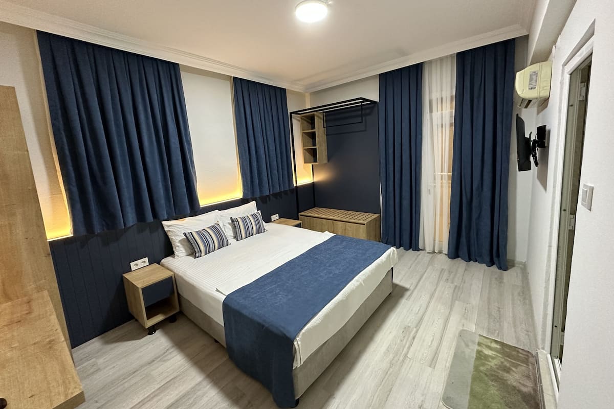 A modern hotel room with a large bed, wooden nightstands, a built-in shelf, and a ceiling light.