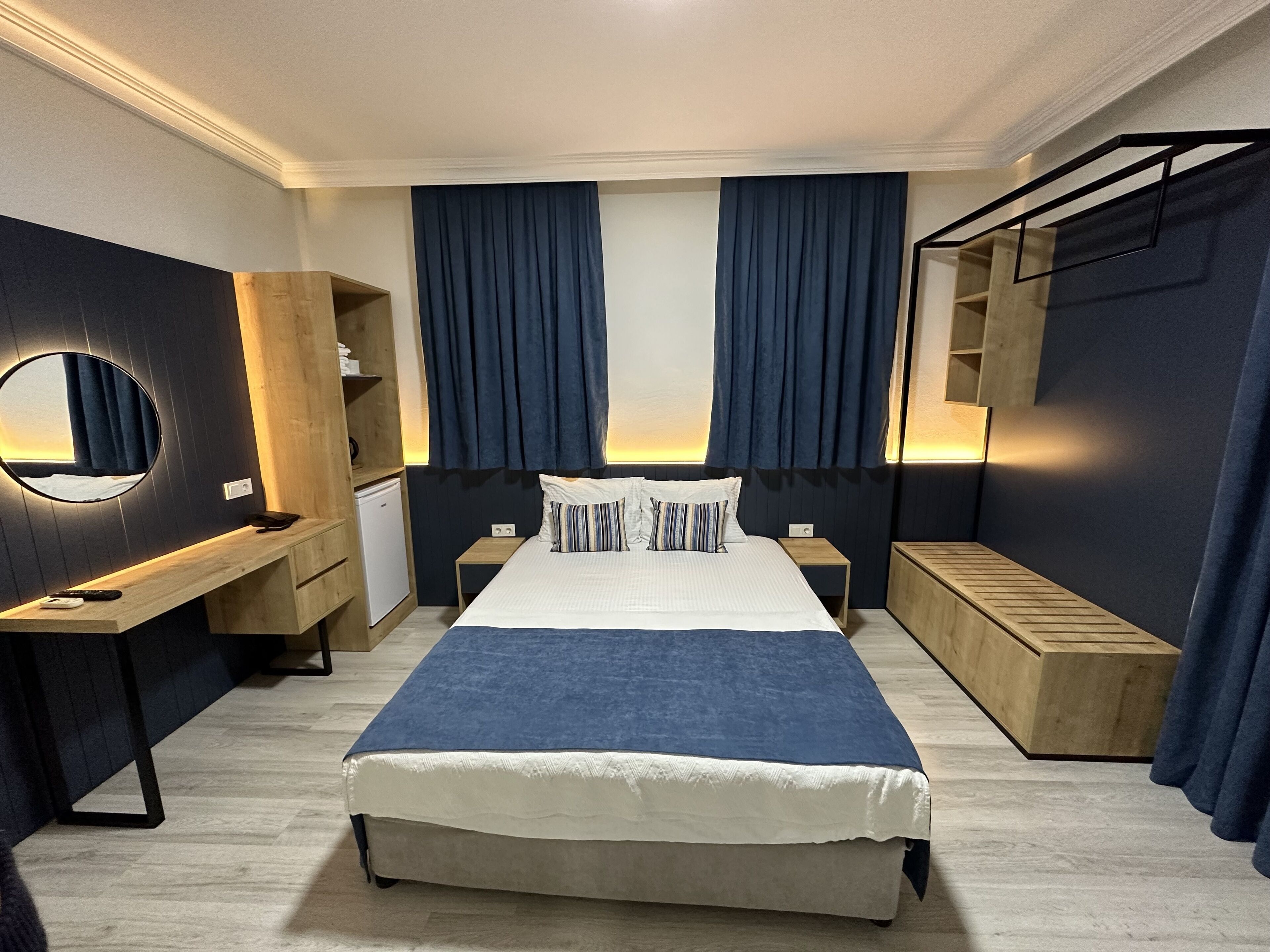 A modern hotel room with a large bed, a bedside table, a mirror, and a wardrobe.