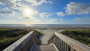 Un muelle de madera que conduce a una playa con el océano al fondo y un cielo parcialmente nublado.