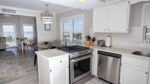 A modern kitchen with white cabinets, stainless steel appliances, and a view to the outside. - Come feel the "SEA BREEZE" - Minimum 2 week rental starting on Sundays (Emerald Isle)