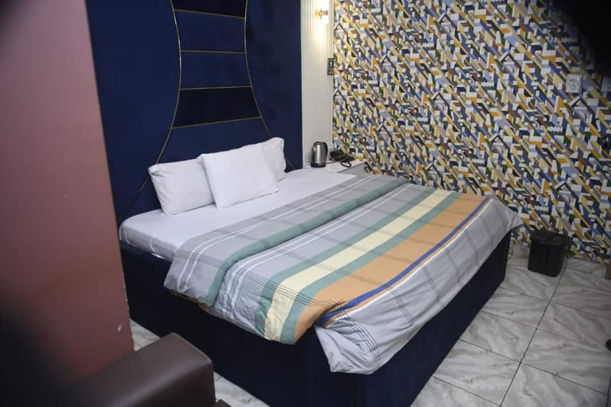 Un lit avec une couvre-lit à rayures, une table de chevet et un mur orné d’un motif.