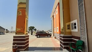 A building entrance with a covered area, a car parked in front, and a green chair near the entrance. - Joclarif Hotel (Zaria)