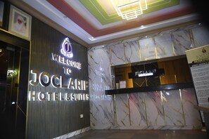 A hotel reception area with a marble wall, a reception desk, and a sign that reads 'WELCOME TO JOCLAIRE HOTEL & SUIRES.' - Joclarif Hotel (Zaria)