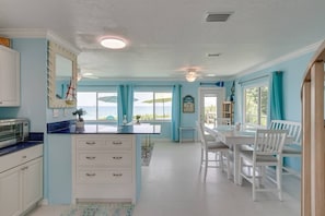 Una cucina luminosa con una grande isola, mobili bianchi e vista sull'oceano.