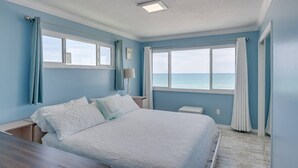 A bedroom with a bed, a nightstand, a lamp, and a view of the ocean. - Charming Two Story House located directly on Melbourne Beach. (Melbourne Beach)