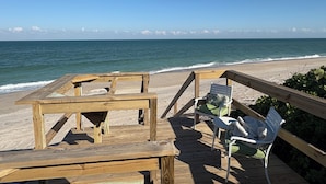 A wooden deck with a table and two chairs overlooking a beach. - Charming Two Story House located directly on Melbourne Beach. (Melbourne Beach)