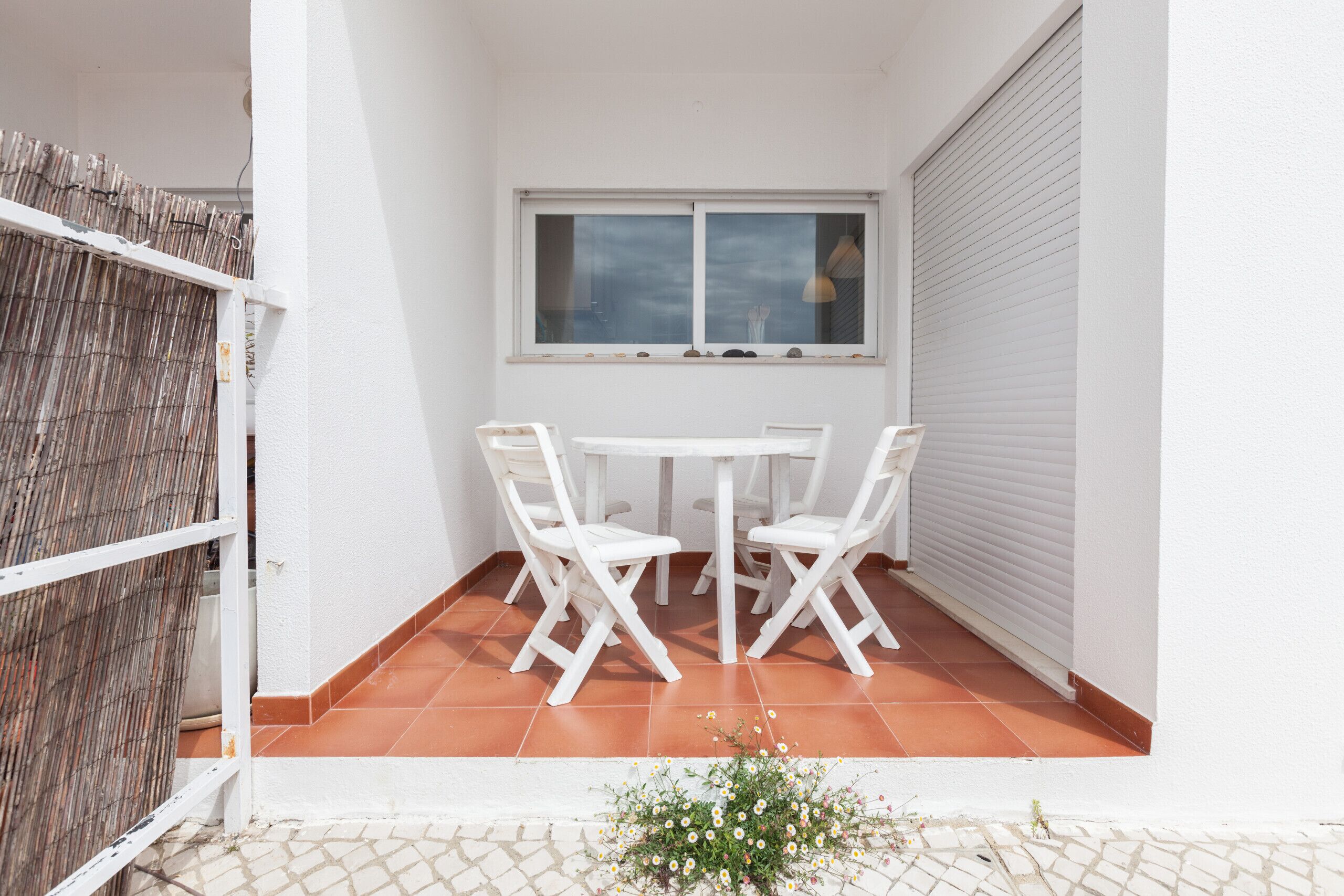 A small patio with a white table and chairs, a window, and a closed roller door.
