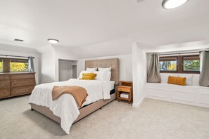 A bedroom with a large bed, a wooden dresser, a nightstand, and a window seat with curtains.