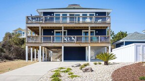A two-story beachfront house with a balcony, a garage, and a small garden area. - Newly Renovated Semi-Oceanfront Duck Home w/Pool (Duck)