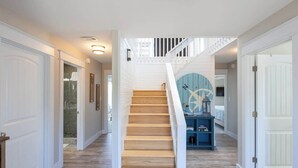 A staircase with wooden steps leading to a landing with a blue console and a wall-mounted compass decoration. - Newly Renovated Semi-Oceanfront Duck Home w/Pool (Duck)
